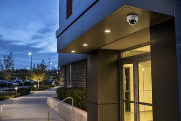 Vandal-resistant dome camera mounted above a building entrance with concealed cabling