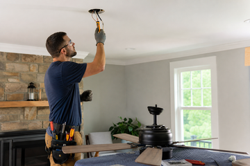 Electrician checking a ceiling fan box with a voltage tester in a Kingston home