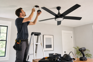Electrician preparing a ceiling fan beside a residential ceiling fixture